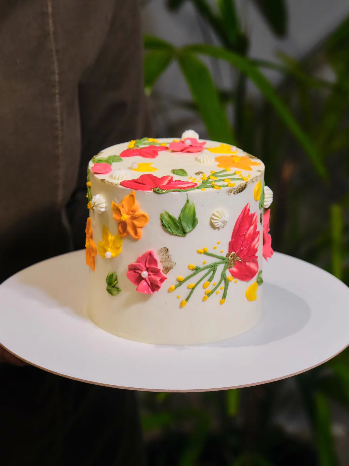 Bolo festivo com cobertura de buttercream branco e pintura artesanal de flores coloridas com folhas de ouro